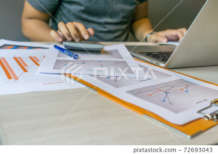 Human hands using calculator next to laptop and graph document Human hands using calculator next to laptop and graph document 72693043
