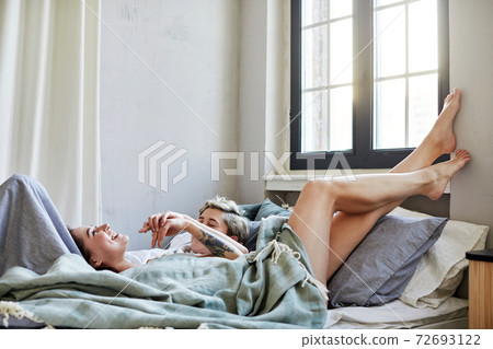 Happy lesbian couple chilling on bed together Happy lesbian couple chilling on bed together 72693122