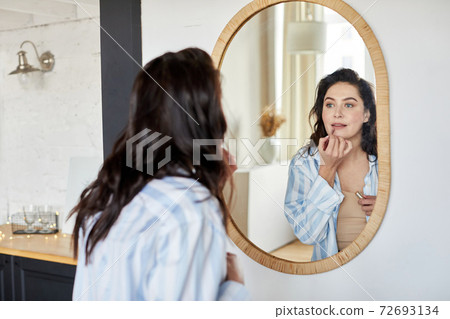 Woman applying makeup near mirror Woman applying makeup near mirror 72693134