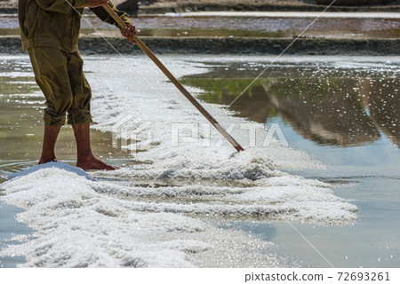 Worker using wooden tool harvesting salt at sea salt farm Worker using wooden tool harvesting salt at sea salt farm 72693261