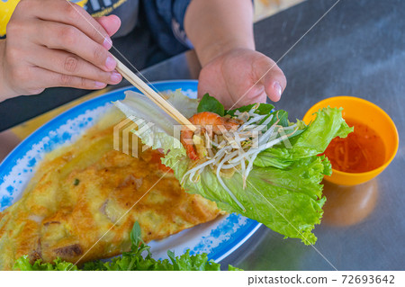 Human eating Banh Xeo crepe with lettuce and fish sauce 72693642