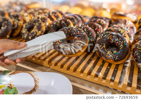 Hand picking chocolate donut by clamp at bakery Hand picking chocolate donut by clamp at bakery 72693659