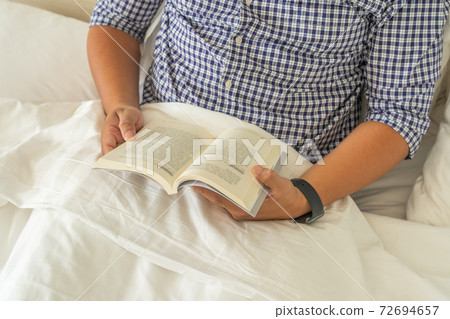 Man hands holding book while reading on bed Man hands holding book while reading on bed 72694657