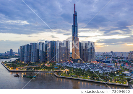Tall buildings on along riverbank under cloudy sky in evening 72694660