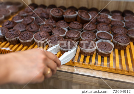 Woman hand picking chocolate muffin by clamp at bakery Woman hand picking chocolate muffin by clamp at bakery 72694912