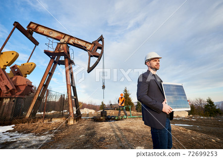 Oil worker in helmet holding solar panel. 72699253