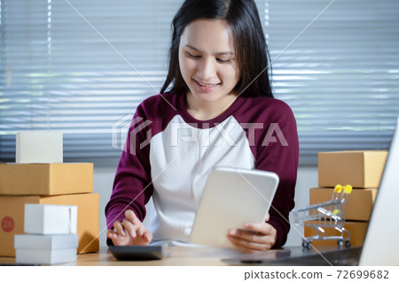 Female seller is checking the number of orders for her products that have been ordered using the tablet. Online Shopping and E-commerce concept. Female seller is checking the number of orders for her products that have been ordered using the tablet. Online Shopping and E-commerce concept. 72699682