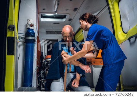 Young nurse wraps a tourniquet around a hand of her patient in an ambulance car 72700242
