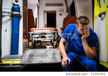 A pensive paramedic sitting on the edge of an ambulance car A pensive paramedic sitting on the edge of an ambulance car 72701455