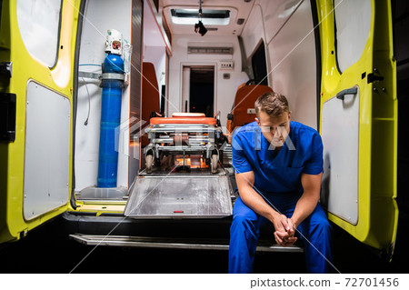 Man in a medical uniform sitting in the ambulance car at night Man in a medical uniform sitting in the ambulance car at night 72701456