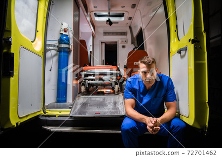Serious man in a medical iniform sitting in the back of an ambulance car Serious man in a medical iniform sitting in the back of an ambulance car 72701462