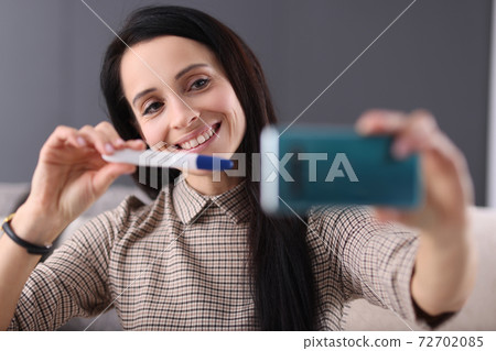Smiling woman shows pregnancy test in smartphone Smiling woman shows pregnancy test in smartphone 72702085