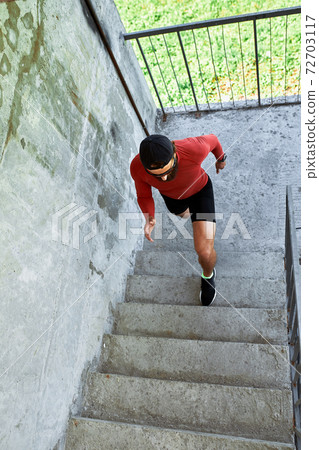 Concentrated male athlete running up stairs to make training more intensive. Sporty handsome young man training alone outdoors. Staircase workout concept Concentrated male athlete running up stairs to make training more intensive. Sporty handsome young man training alone outdoors. Staircase workout concept 72703117
