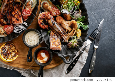 grilled seafood platter. Assorted delicious grilled seafood with vegetables. Grilled mixed bastards with pepper sauce and vegetables. Black background grilled seafood platter. Assorted delicious grilled seafood with vegetables. Grilled mixed bastards with pepper sauce and vegetables. Black background 72703120