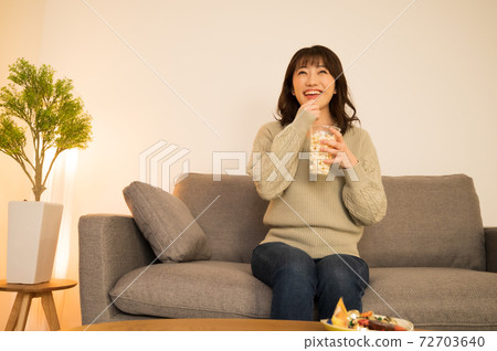 A woman enjoying TV while holding popcorn A woman enjoying TV while holding popcorn 72703640