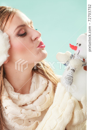 Cute woman kissing little snowman. Winter fashion. 72703782