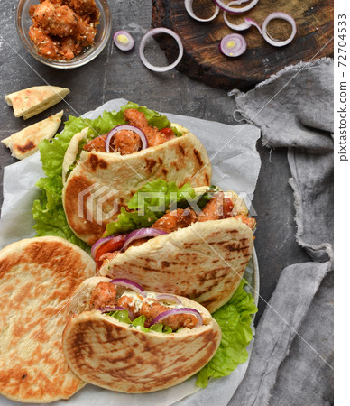 Lavash salad with fried chicken and vegetables. Pita with chicken nuggets, tomatoes, red onions and lettuce and sauce. Healthy fast food. Top view. Dark background. Lavash salad with fried chicken and vegetables. Pita with chicken nuggets, tomatoes, red onions and lettuce and sauce. Healthy fast food. Top view. Dark background. 72704533