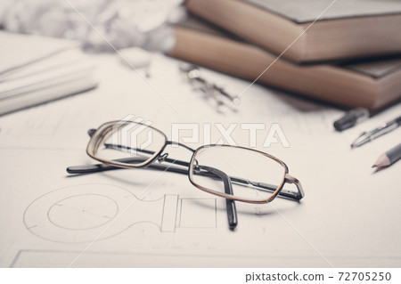 Glasses next to books, compass and pencils 72705250