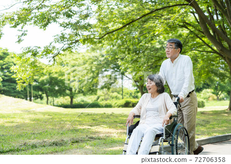 Senior couple walking in a wheelchair Senior couple walking in a wheelchair 72706358