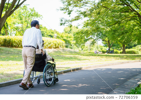 Senior couple walking in a wheelchair Senior couple walking in a wheelchair 72706359