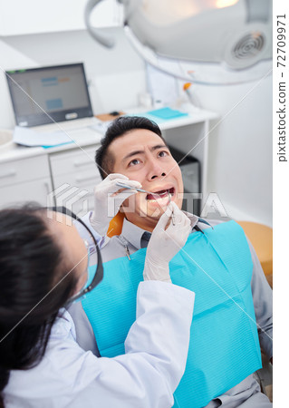 Checking teeth of scared man Checking teeth of scared man 72709971