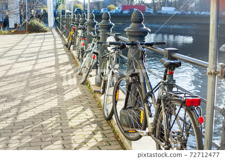 Several multi-colored bicycles are fastened to the wrought-iron fence on the embankment. 72712477