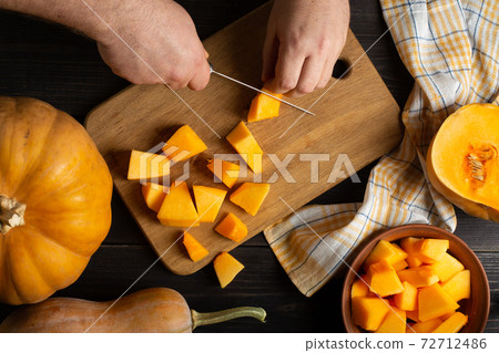 The cook cuts the pumpkin into pieces for baking. Top view. The cook cuts the pumpkin into pieces for baking. Top view. 72712486