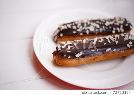 two eclairs on a white plate on a light wooden background two eclairs on a white plate on a light wooden background 72713394