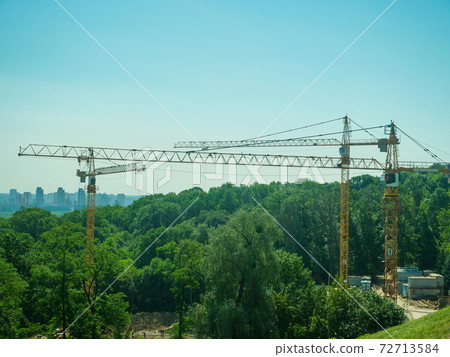 Construction cranes on the outskirts of the city. Destruction of forests by construction. Construction cranes on the outskirts of the city. Destruction of forests by construction. 72713584
