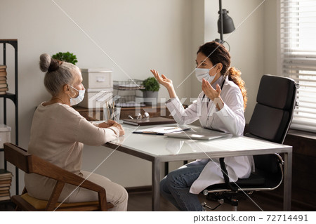 Female doctor and elderly patient in facial masks 72714491