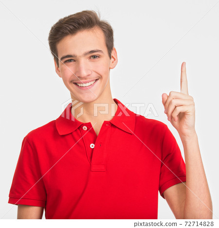 Portrait of happy young man pointing up buy finger, isolated over white background. Photo of smiling  Handsome white guy in a red shirt showing index finger.  Male person with an idea gesture. 72714828