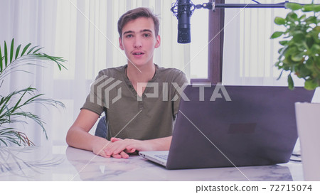 Man blogger videotapes his vlog at home. Teenage boy recording his video blog. Young man speaks in front of a video camera for his blog channel. Vlogger makes online streaming using smartphone 72715074