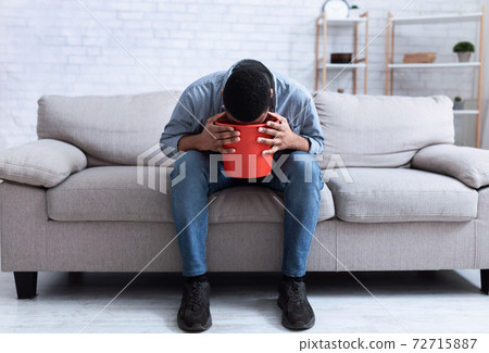 African Man Vomiting Into Bucket Sitting On Couch At Home 72715887