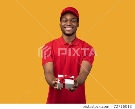Black delivery man holding gift box giving it to camera Black delivery man holding gift box giving it to camera 72716018