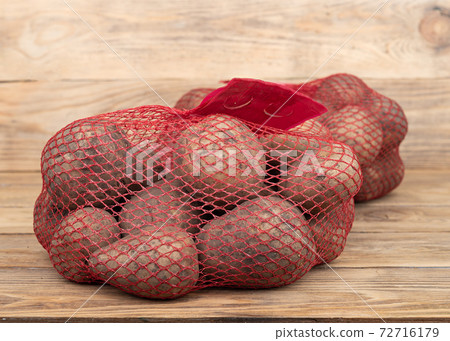 Two red nets with potatoes on a wooden background. 72716179