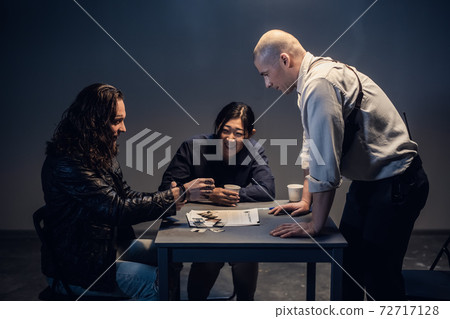 A police detective at the station and his partner, an asian woman, present evidence to a male suspect in an interview room. A police detective at the station and his partner, an asian woman, present evidence to a male suspect in an interview room. 72717128