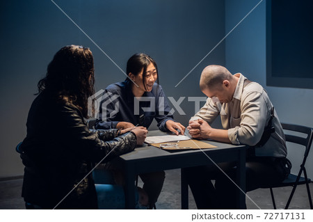 The murder suspect is in the interrogation room with a grim investigator and lawyer. 72717131
