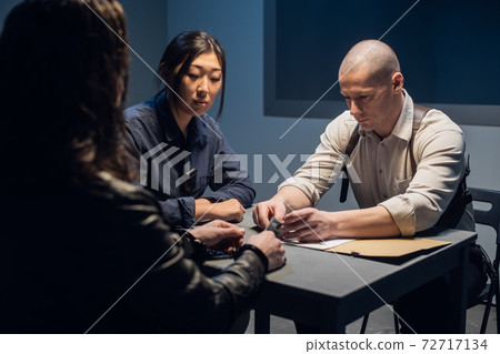 Two police officers a man and a woman are questioning the alleged offender at the police station Two police officers a man and a woman are questioning the alleged offender at the police station 72717134