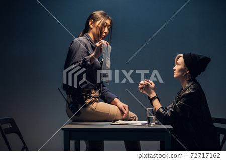 An experienced investigator during an interrogation at a police station shows the criminal girl the found crime weapon An experienced investigator during an interrogation at a police station shows the criminal girl the found crime weapon 72717162