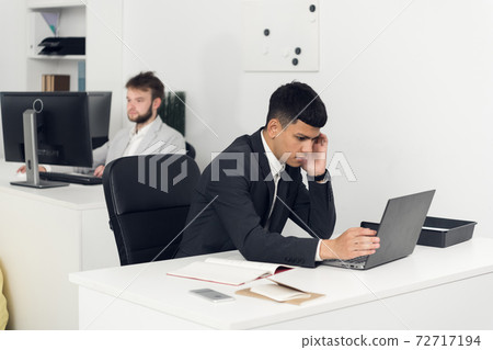 The Manager is busy with office work at a Desk in the open-space office of a large company. The Manager is busy with office work at a Desk in the open-space office of a large company. 72717194