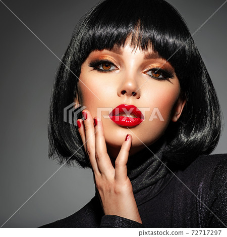 Beautiful brunette girl with red lips. Pretty young sensual woman with red nails. Closeup portrait of a model with bright makeup on a face. Attractive female posing at studio. 72717297
