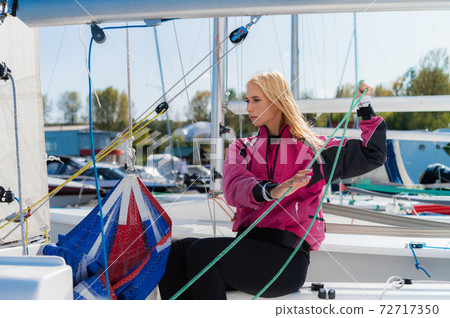 A young female sailing athlete sets a genaker sail on her white sports yacht to go to a regatta. 72717350