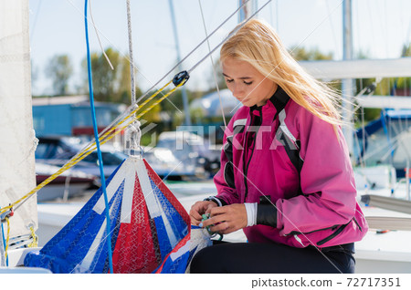 A young female sailing athlete sets a genaker sail on her white sports yacht to go to a regatta. 72717351