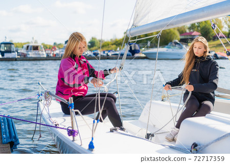 Two young blonde girls on a sunny summer day on a sailing boat are preparing for a river trip 72717359