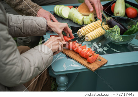 Joyful efforts to prepare for a family holiday in the yard. Hands of a man and a woman preparing vegetables for grilling for a picnic. Without a face. 72717442