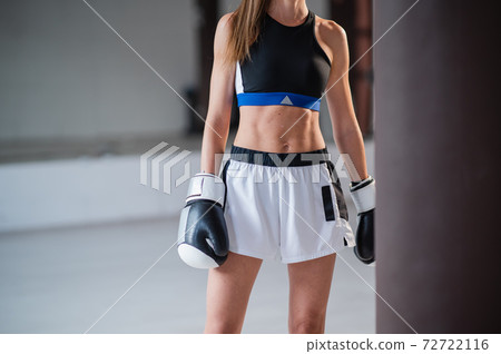 The body of a young slender athlete kickboxer without a face with a pumped up press in a sports uniform and gloves in the gym with a punching bag The body of a young slender athlete kickboxer without a face with a pumped up press in a sports uniform and gloves in the gym with a punching bag 72722116