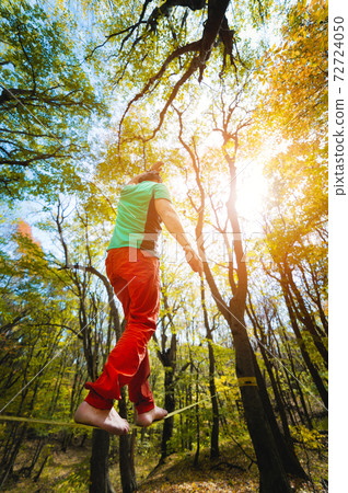 An adult bearded man balancing on a tight slackline is engaged in balancing act in the autumn forest 72724050