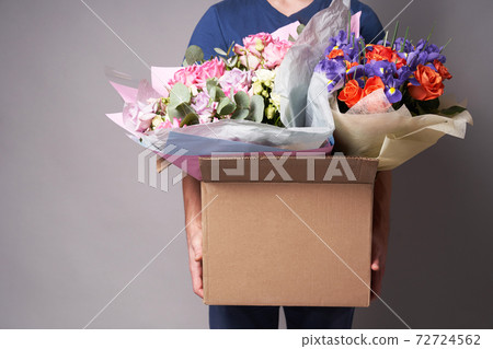 White male courier holding a large cardboard box with several bouquets, White male courier holding a large cardboard box with several bouquets, 72724562