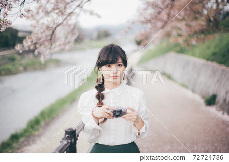 Woman in white shirt with cherry blossom background and camera 72724786