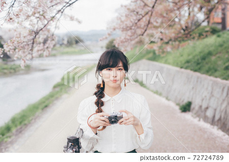 Woman in white shirt with cherry blossom background and camera 72724789